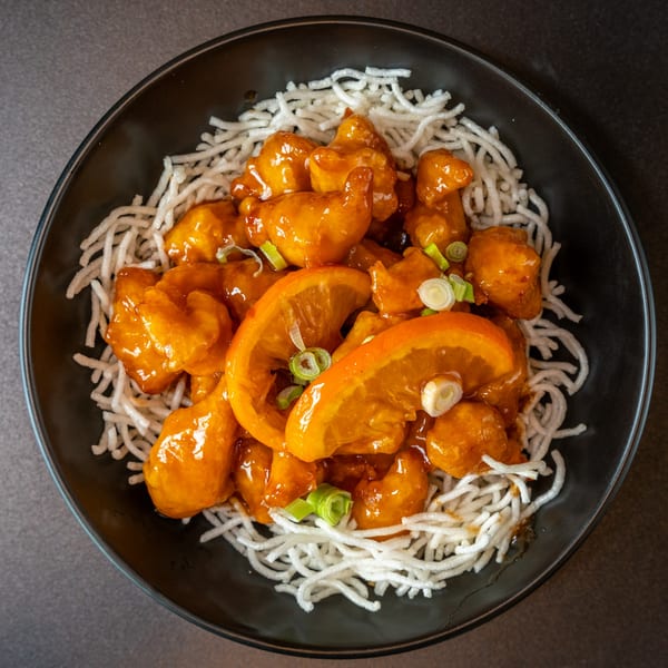 Yen Ching Express orange chicken with crispy noodles, garnished with orange slices and green onions.