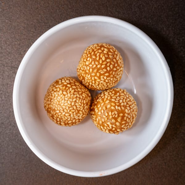 Three golden-brown sesame balls, a Chinese dessert, are served in a white bowl.